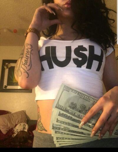 A woman holding money in her hand and wearing a shirt with the word " hush ".